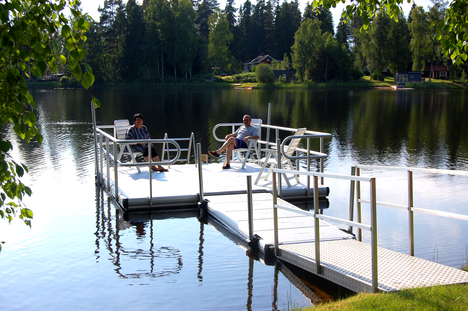 Två personer sitter på en EasyFloat privat badbrygga med solstolar och räcken runtom, som en terrass eller altan.
